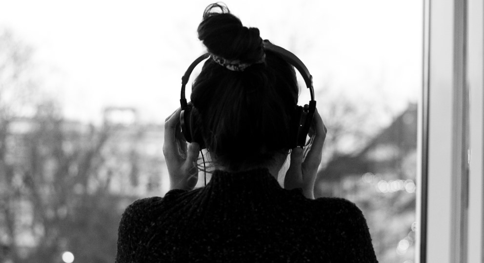 Frau steht am Fenster, hört Musik mit Kopfhörern