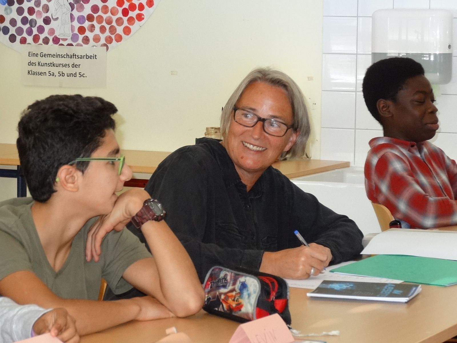 Jutta Reichelt sitzt neben einem Schüler, lächelt ihn an und schreibt etwas