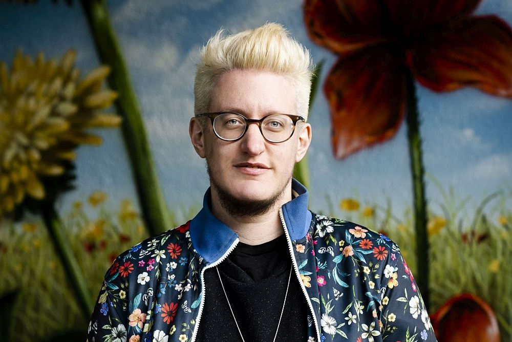 Linus Giese in einer bunten Jacke vor einem bunten Hintergrund