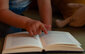 Foto eines aufgeschlagenen Buchs, darüber der Finger eines Kleinkinds, das darin liest